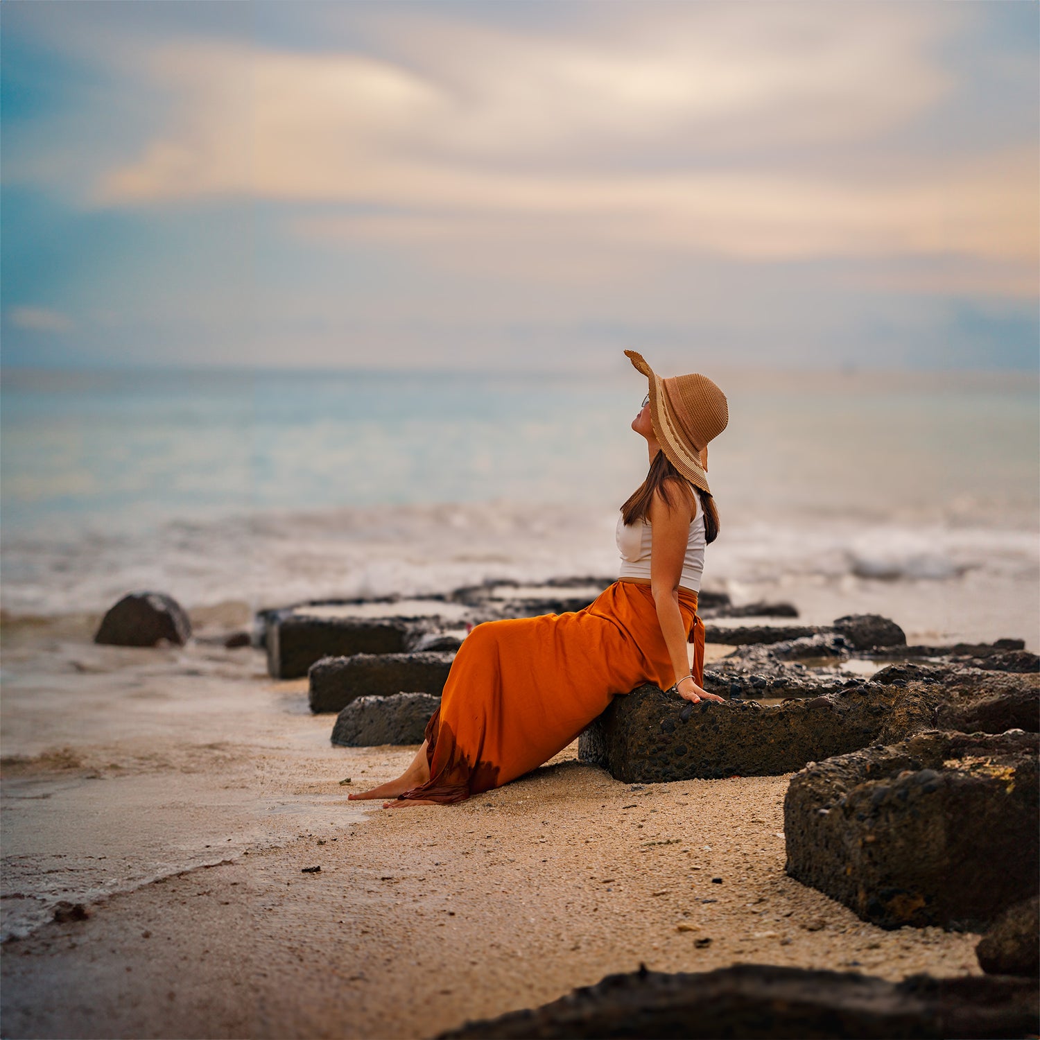A woman sitting on a wave breaker at the beach, gazing into the distance with her hair gently tousled by the ocean breeze, embodying a moment of tranquility and connection with nature.